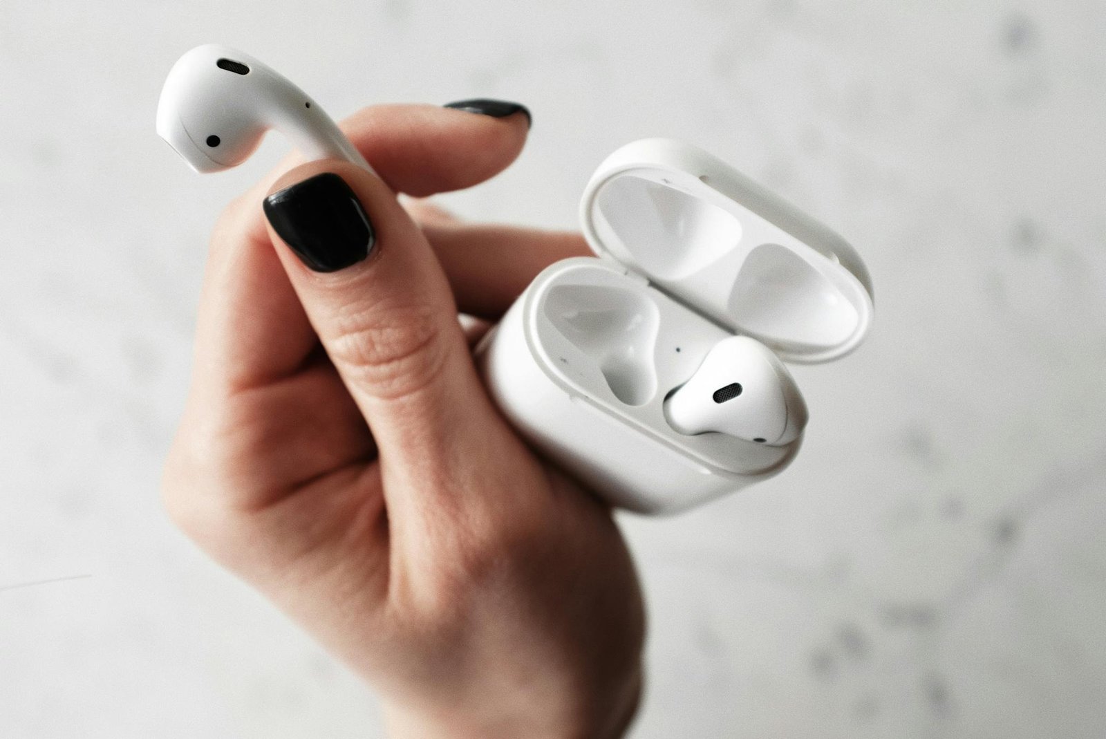 Home 2 A detailed close-up of white wireless earbuds held in a hand with black nail polish.