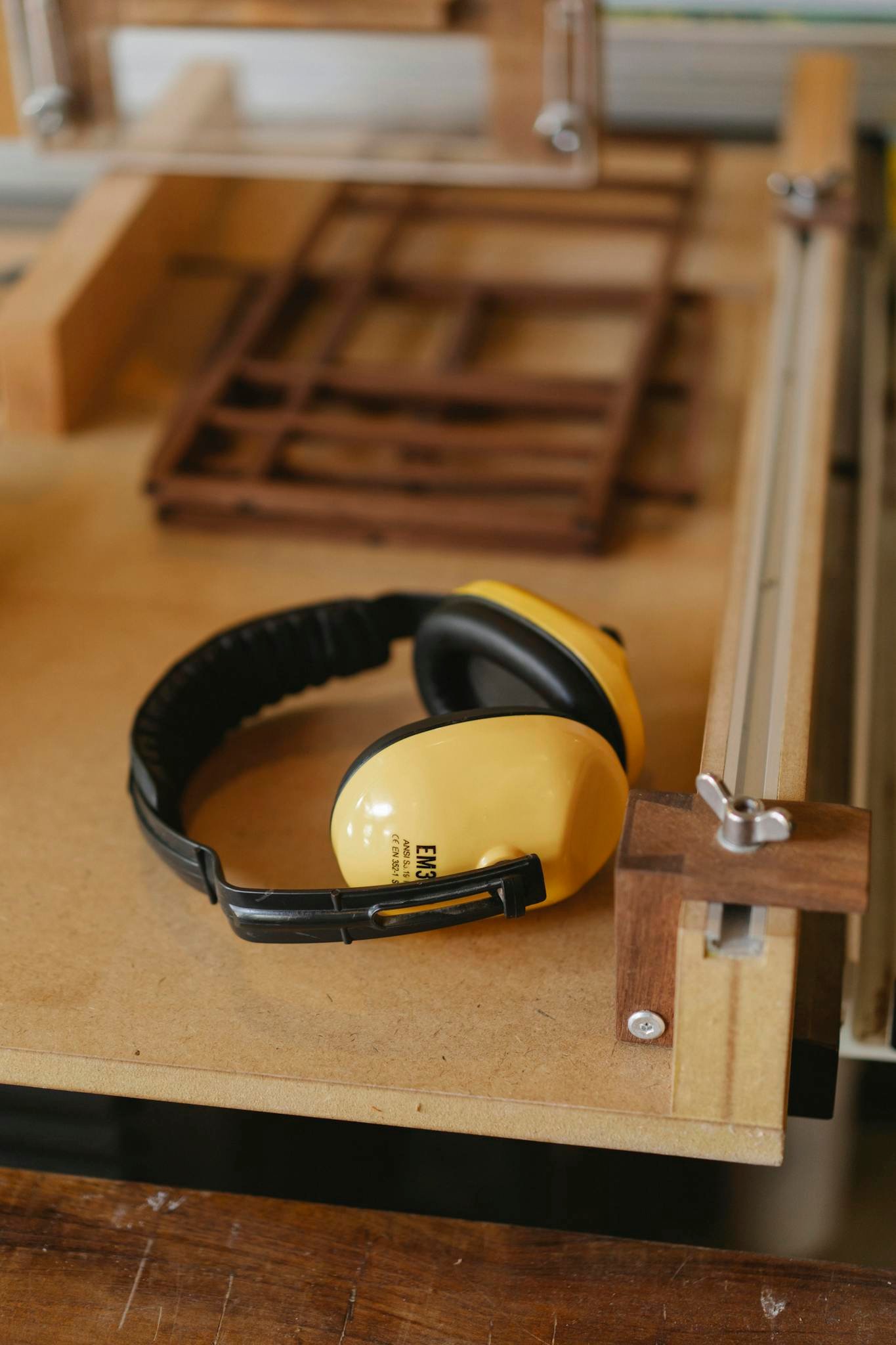 About 1 Yellow noise-cancelling headphones placed on a carpentry workbench in a workshop setting.